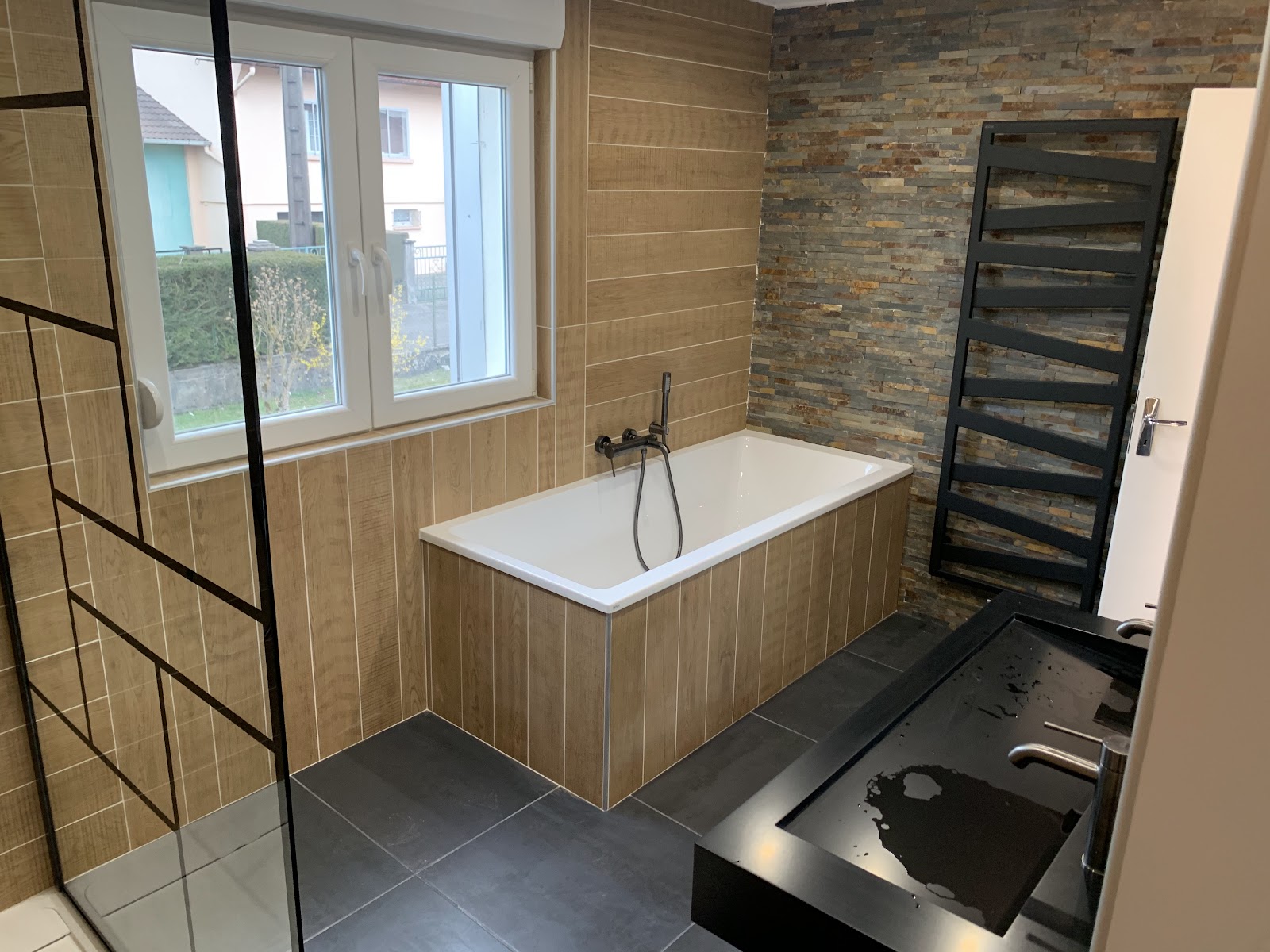 Salle de bain moderne avec baignoire habillée de bois et mur en pierre à Belfort.